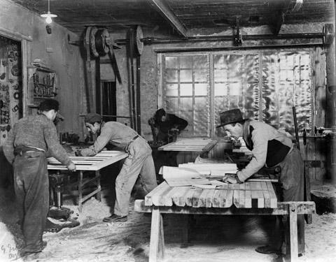 Il Cav. Navello Sebastiano (a destra) sta leggendo dei progetti di costruzione dei serramenti, sulla sinistra degli operai stanno passando alla macchina “Toupie” un serramento per eseguire la “squadratura” del battente (1940)